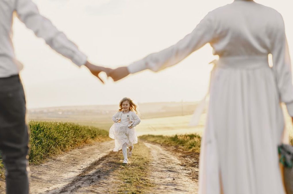 A joyful child runs toward parents holding hands on a sunny rural path.